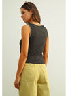 Woman wearing a dark gray sleeveless top with white trim and light green pants on a light background