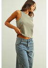 Woman wearing a green tank top and blue jeans on a plain background