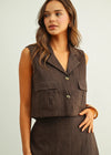Woman wearing a brown vest over a matching skirt against a plain background