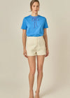 Woman wearing a blue top and beige shorts on a plain background