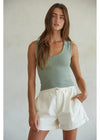 Woman wearing a green tank top and white shorts against a neutral background
