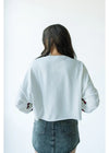 Person wearing a white cropped sweatshirt with red accents on a plain background