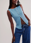 Woman wearing a blue ribbed top with button details and blue jeans on a plain background