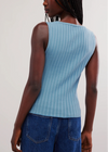 Person wearing a light blue ribbed tank top and blue jeans on a plain background