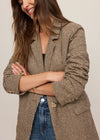 Woman wearing a brown checkered blazer over a black top and blue jeans on a plain background