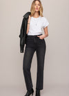 Woman wearing a white t-shirt, black jeans, and a black leather jacket on a beige background