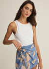 Woman wearing a white sleeveless top and blue floral skirt on a beige background