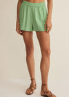 Person wearing light green shorts on a beige background