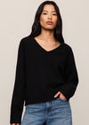 Woman wearing a black sweater and blue jeans against a beige background