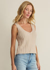 Woman wearing a beige ribbed tank top and light blue jeans against a plain background
