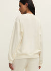 Person wearing a cream-colored sweater and pants on a plain background