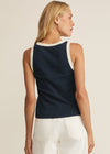 Woman wearing a navy sleeveless top with lace trim and white shorts on a beige background
