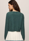 Woman wearing a green sweater and white skirt with a beige background
