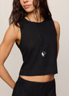 Woman wearing a black sleeveless top and skirt with a necklace on a plain background
