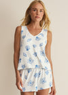 Woman wearing a white sleeveless top and shorts with blue floral and shell pattern on a beige background