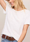 Woman wearing a white t-shirt and blue jeans with a brown belt against a plain background