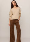Woman wearing a beige sweater and brown pants on a plain background