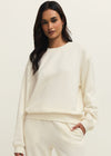 Woman wearing a white sweater and pants against a plain background