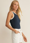 Woman wearing a navy tank top with lace trim and white shorts on a beige background