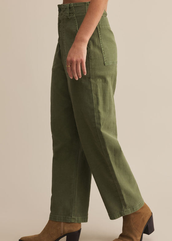 Person wearing green pants and brown boots on a beige background