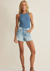Woman wearing a blue tank top and denim shorts on a beige background