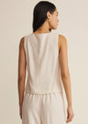 Woman wearing a beige sleeveless top and pants on a plain background