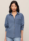 Woman wearing a blue denim shirt and light blue jeans on a beige background