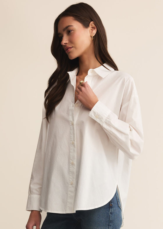 Woman wearing a white shirt and blue jeans against a beige background