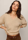 Woman wearing a beige sweater and brown pants against a plain background